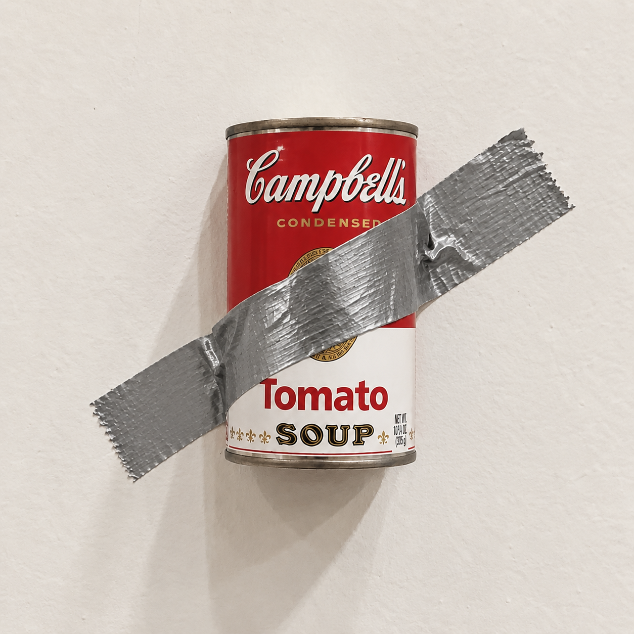 A Campbell's soup can fixed to a gallery wall with silver duct tape
